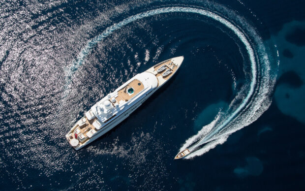 A luxury yacht cruising in the deep blue sea with a speedboat creating a curved trail behind
