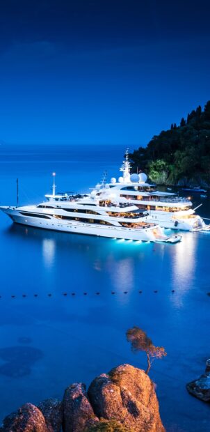 Luxury yacht sailing near rocky coastline under blue evening sky