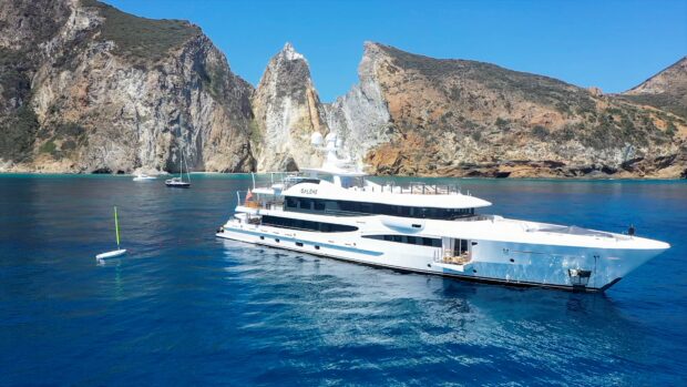 A luxury yacht cruising near rocky cliffs under a clear blue sky in bright sunlight