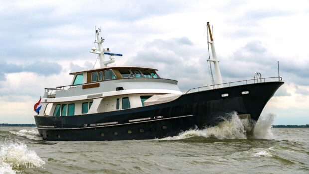 A luxury yacht cruising through choppy waters on a cloudy day with a Dutch flag flying