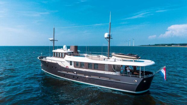 A luxurious yacht sailing on calm blue ocean waters with wind turbines in the background