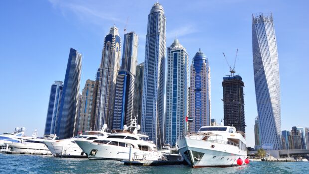 Luxury yacht docked in marina with city skyscrapers in the background at clear blue sky