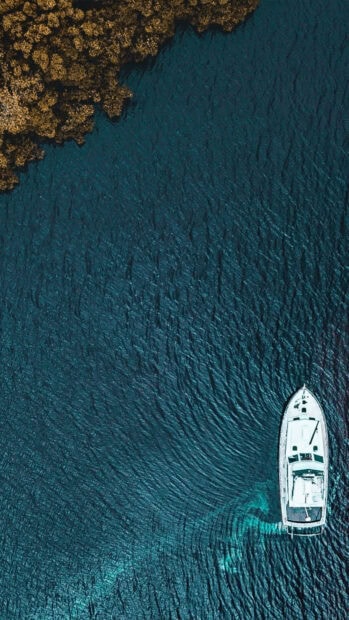 Aerial view of yacht cruising near a rocky coastline in clear blue water