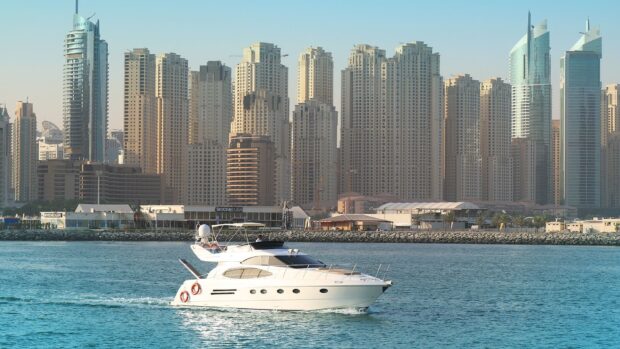A luxury yacht cruising on blue water near tall city skyscrapers in clear daylight