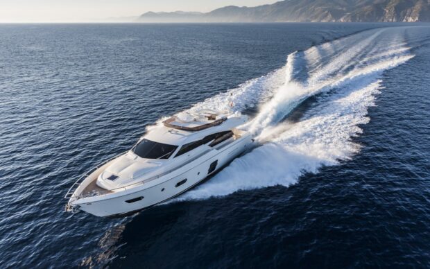 A luxury yacht cruising on the deep blue ocean near the coastline creating white waves behind