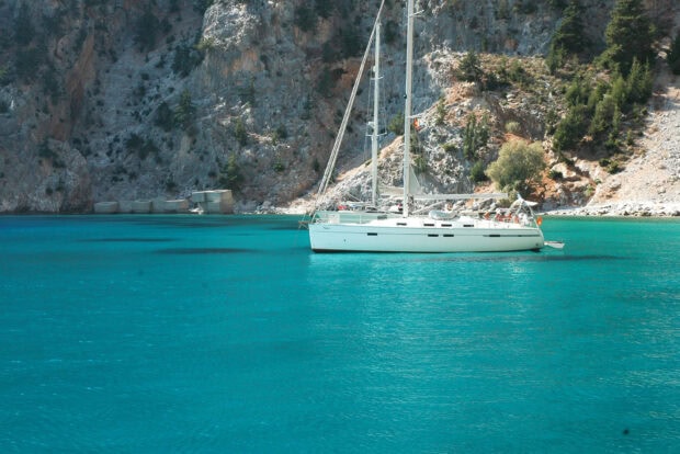 A yacht sailing on clear turquoise water near rocky cliffs in a peaceful bay