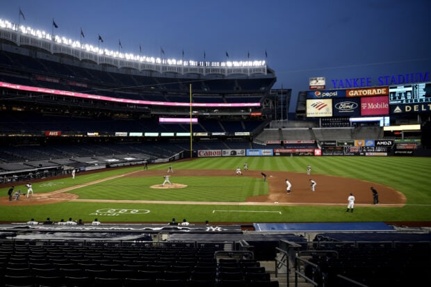A baseball game at Yankee Stadium during twilight with players on the field and illuminated stadium lights