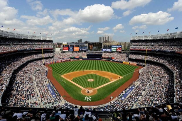 A crowded baseball field at Yankee Stadium with players and fans on a sunny day