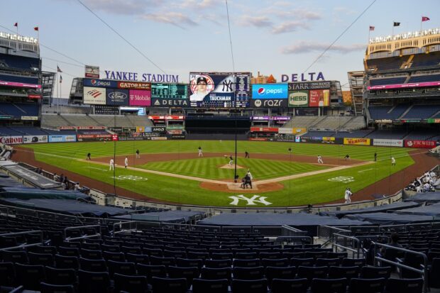 A panoramic view of Yankee Stadium during a baseball game at sunset with players on the field and the scoreboard visible