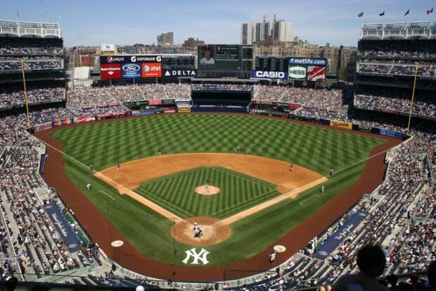 A wide view of Yankee Stadium during a baseball game with players on the field and a packed crowd
