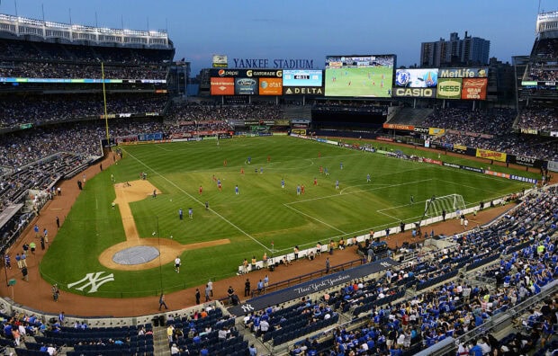 A sports match is taking place on the field at Yankee Stadium filled with fans in the stands