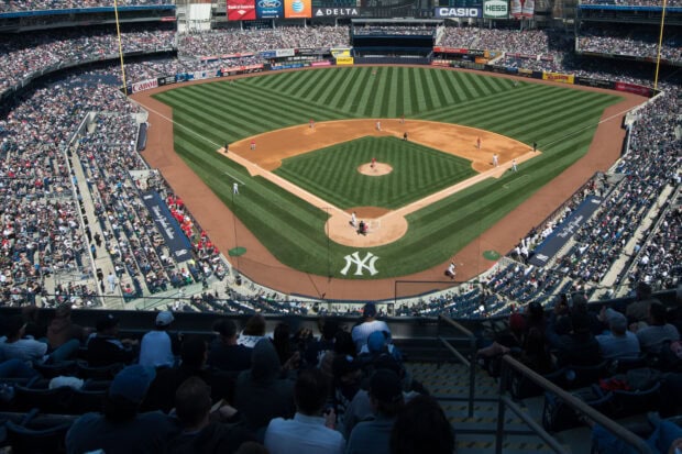 A wide view of Yankee Stadium from the stands showing the baseball field and players on the field