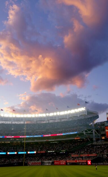 Evening sky over Yankee Stadium with vibrant clouds and a crowded field during a game