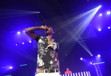 Young Dolph performing on stage with microphone and floral shirt under bright purple lights