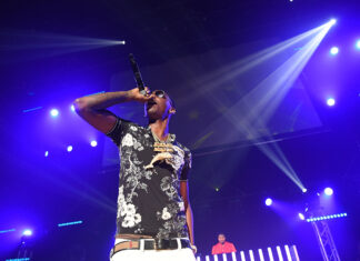 Young Dolph performing on stage with microphone and floral shirt under bright purple lights