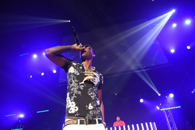 Young Dolph performing on stage with microphone and floral shirt under bright purple lights