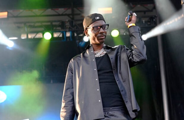 Young Dolph wearing a black jacket and glasses while performing on stage