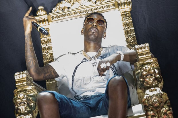 Young Dolph sitting on a golden throne wearing sunglasses and chains