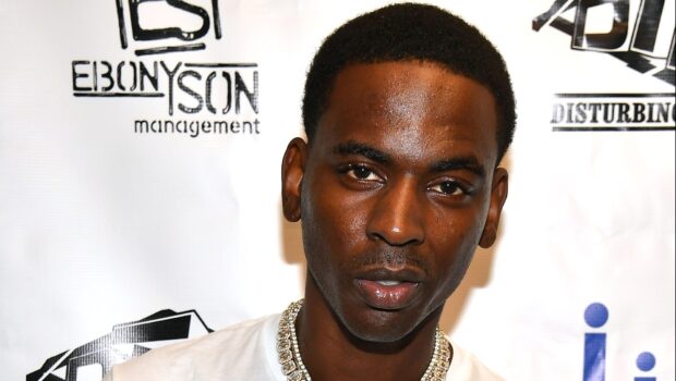 Young Dolph wearing a diamond chain with a white shirt at an event with logos in the background