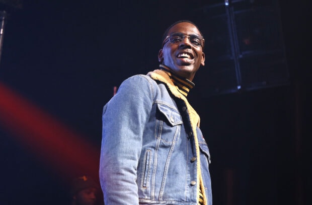 Young Dolph wearing a denim jacket with fur collar smiling on stage