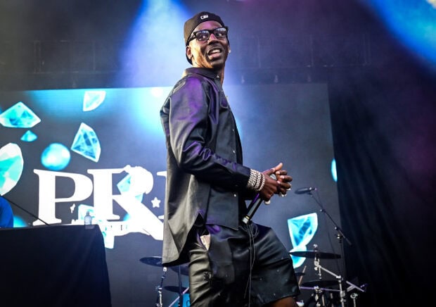 Young Dolph performing on stage wearing a black outfit with jewelry and sunglasses