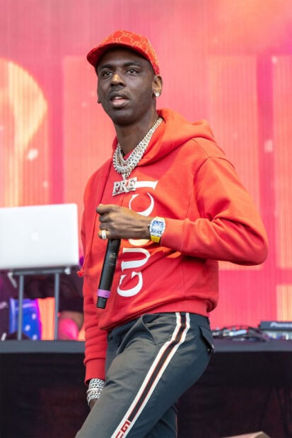 Young Dolph wearing a red hoodie and holding a microphone on stage at a concert