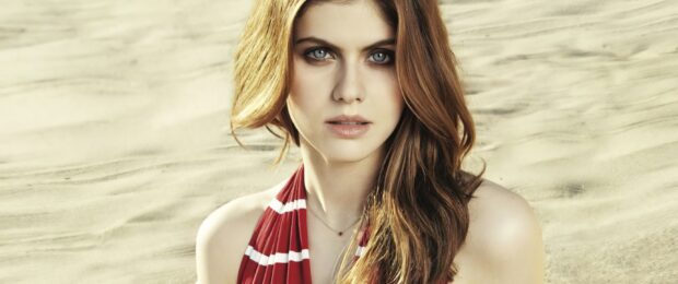 Alexandra Daddario with blue eyes wearing a red striped top in a sandy environment