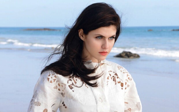 Alexandra Daddario wearing a white lace dress standing by the ocean at the beach
