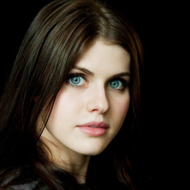 Alexandra Daddario with blue eyes and brown hair looking at the camera with a black background