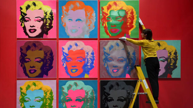 A woman arranging colorful Andy Warhol art pieces featuring Marilyn Monroe in a gallery setting