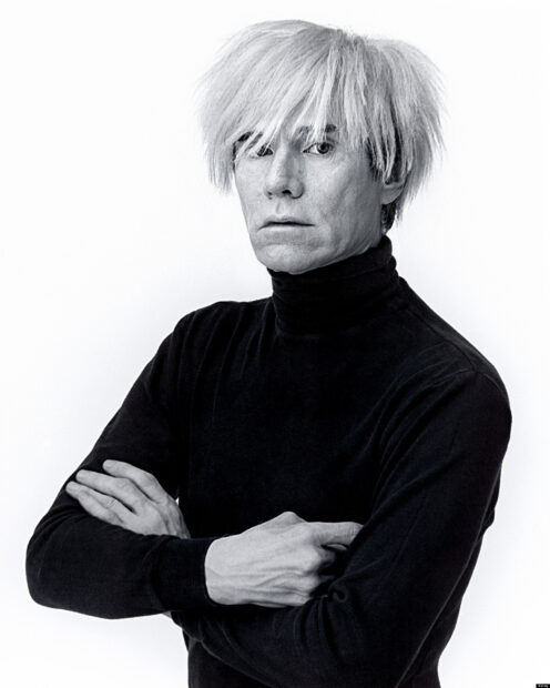 Black and white portrait of Andy Warhol with folded arms and distinctive hairstyle