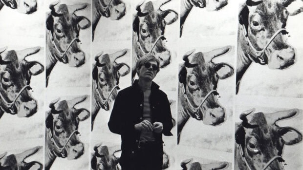 Andy Warhol standing in front of multiple cow images in a black and white setting