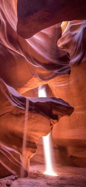 Beam of light inside Antelope Canyon with smooth sandstone walls and sandy ground