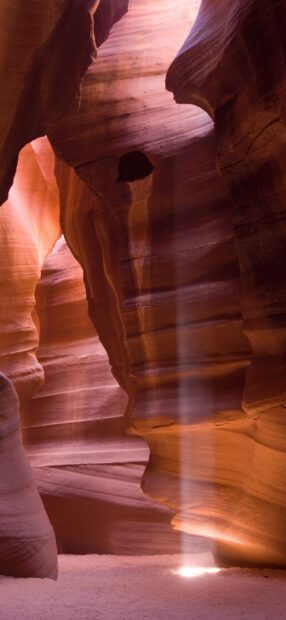 A narrow beam of light shining through Antelope Canyon rock formations in warm hues