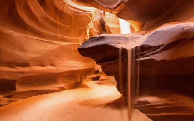 Smooth sandstone formations inside Antelope Canyon with light beams and flowing sand