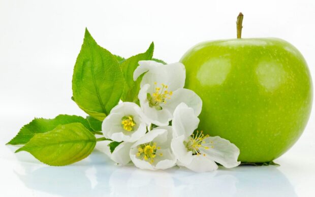 Fresh green apple fruit with white apple blossoms and green leaves on white surface