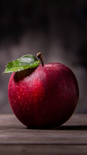 A fresh red apple fruit with a green leaf on top placed on a wooden surface