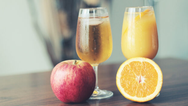 A fresh red apple and citrus fruit with two glasses of juice on a wooden table