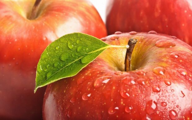 Close up of fresh apple fruit with water droplets and a green leaf
