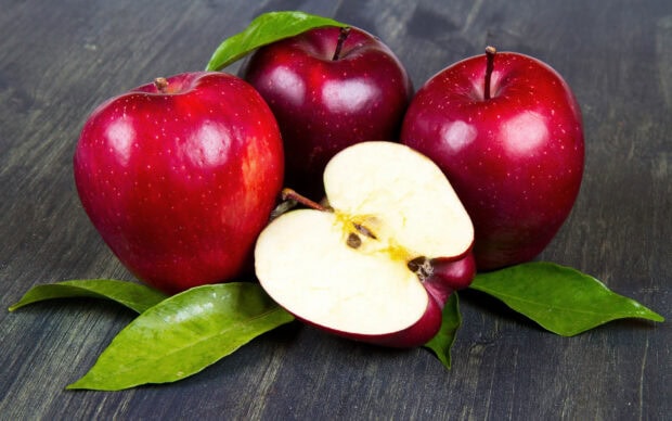 Fresh apple fruit with leaves on a wooden surface showing a cut apple half