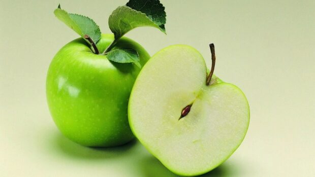 Fresh green apple fruit with one sliced half and leaves on a light background