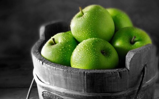 Fresh green apples with water droplets in a wooden bucket bowl