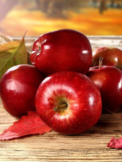 A close up of fresh red apple fruit on wooden surface with autumn leaves