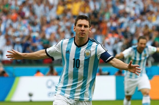 Lionel Messi wearing Argentina jersey celebrating a goal on the football field with a cheering crowd in the background