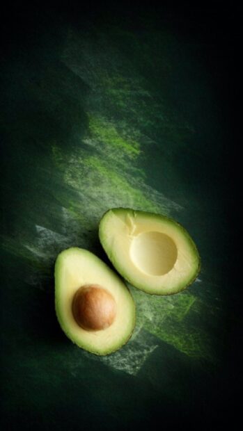 Fresh avocado halves with seed and smooth green flesh on dark textured surface