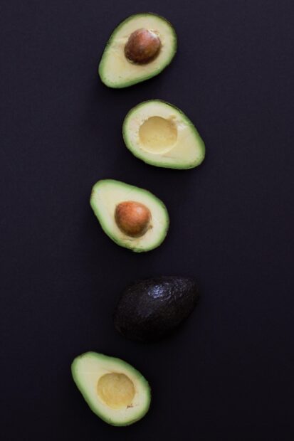 Fresh avocado halves and whole avocado on a dark surface arranged vertically