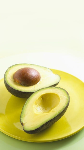 Fresh avocado cut in half with seed on a yellow plate