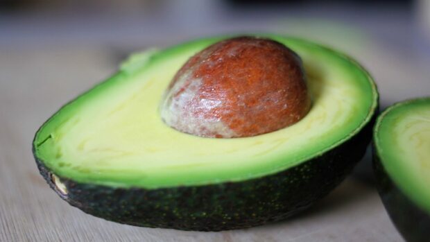 Half of a ripe avocado with seed on a wooden surface