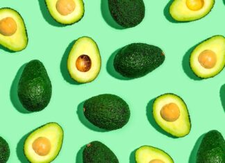 Whole and halved fresh avocado pattern on green surface with avocado fruit