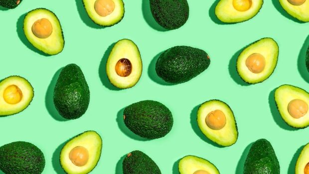 Whole and halved fresh avocado pattern on green surface with avocado fruit